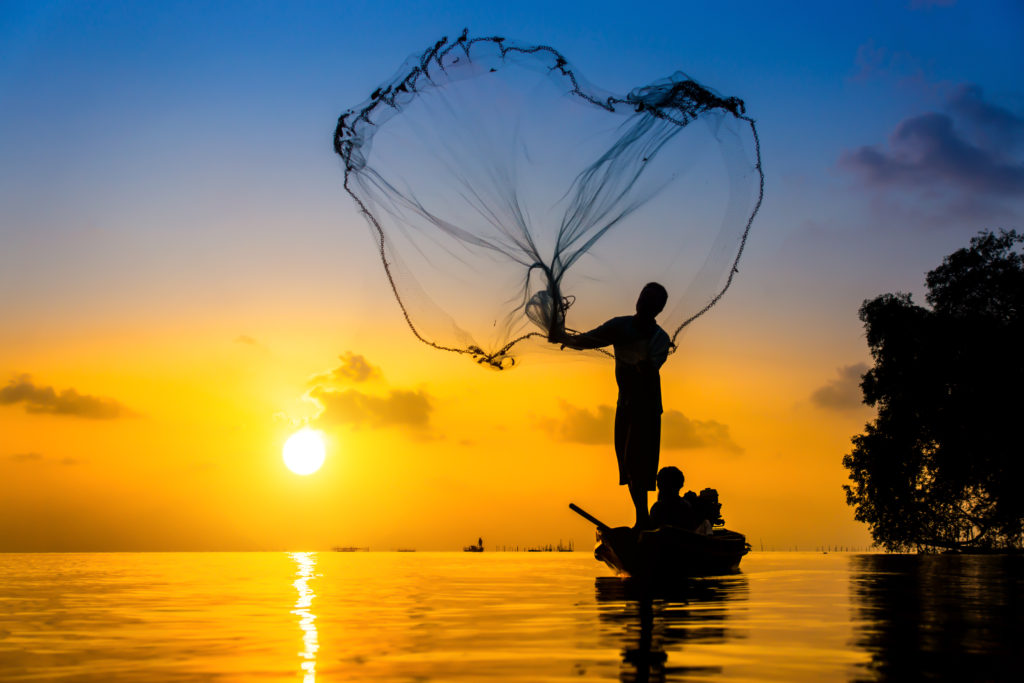 a man casting a net into water.